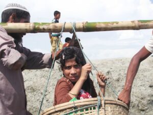Un homme porte une fille Rohingya dans un panier suspendu par une perche en bambou, dans un camp de Cox’s Bazar au Bangladesh.